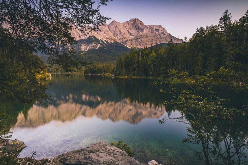 Eibsee Rundweg – ruhiger Eibsee mit Spiegelung der Zugspitze, Wald und Felsen am Ufer in Bayern.