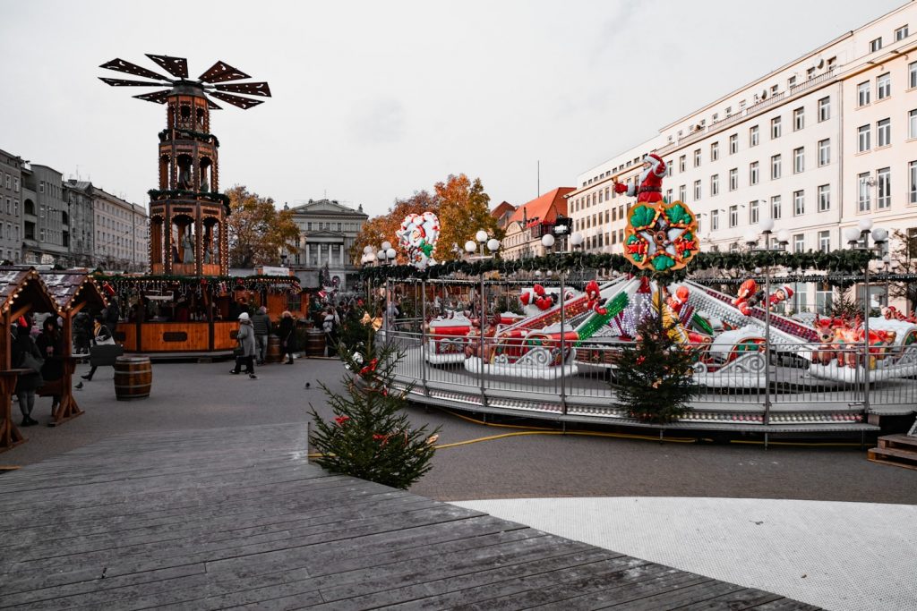 Weihnachtsmarkt Dessau-Roßlau bei Abenddämmerung mit beleuchteten Holzbuden, großem Weihnachtsbaum und Besuchern mit Glühwein in winterlicher Atmosphäre