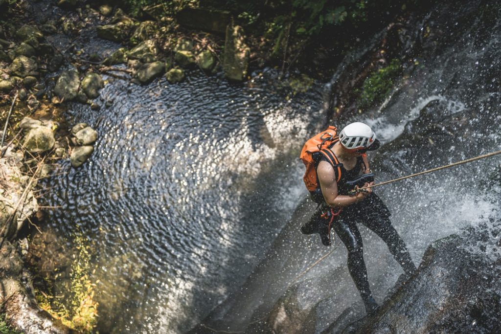 Canyoning mit Kindern Allgäu: Familie mit Guide – Kinder in Neopren und Helm in einer Schlucht mit Bachlauf, Felsen und kleinen Wasserfällen.